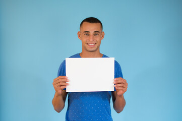 Handsome young man is holding a sheet of paper on blue background