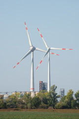 Pair of big wind turbines to generate electrical power and high voltage power lines at blue sky..