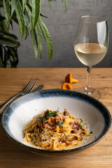 Pasta with wild forest mushrooms and rich cream sauce with a glass of wine, top view on wooden background