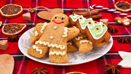 Christmas greeting card. Gingerbread men with fir shaped cookie in a plate, sugar hearts, dried orange slices and spices on a red fabric background.