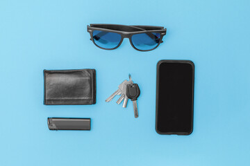 modern man items don't forget to carry in top view on table cell phone sunglasses lighter wallet keys in black on blue background with copy space left