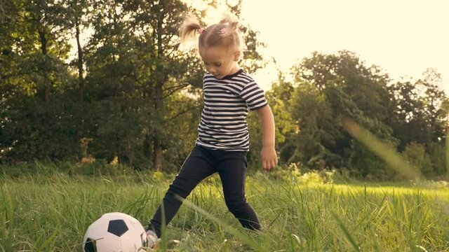Little girl plays with a soccer ball in the park. The child dreams of football. Happy child kicks a ball on a green lawn. Dream concept, happy childhood. Kid in the park outdoors.