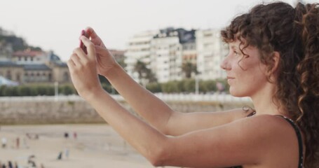 
Curly-haired tourist woman takes photos with her smartphone in the city of San Sebastian, Spain. Cultural tourism . - Powered by Adobe