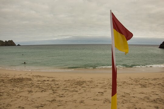 Lifeguard's yellow and red flag marking bathing swimming area on Porthcurno beach in Cornwall UK
