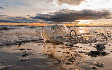 Bouteille en verre échouée sur une plage avec reflets sur le sable et coucher de soleil.