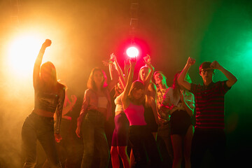 Shadows. A crowd of people in silhouette raises their hands, dancing on dancefloor on neon light...