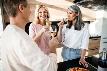 Smiling man and two women with wine glasses on the kitchen