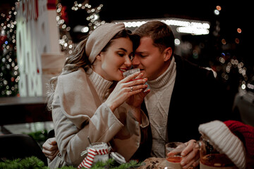 Couple in love relationship believe in meracle, kissing against the chrismas decoration outdoor in the eve, look at each other and drink the warm drinks