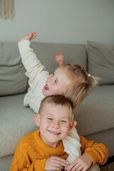 Little brother and sister in cozy knitted sweaters play at home. Portrait of cute little brother and sister. Fall.