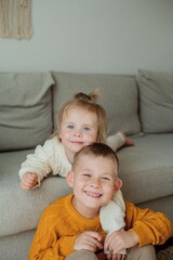 Little brother and sister in cozy knitted sweaters play at home. Portrait of cute little brother and sister. Fall.