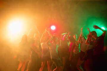Obraz premium Carefree. A crowd of people in silhouette raises their hands, dancing on dancefloor on neon light background. Night life, club, music, dance, motion, youth. Bright colors and moving girls and boys.