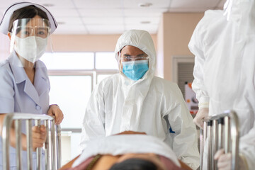 Front view of doctor and medical staff wearing protective face mask in a hurry taking patient on bed to operation room in hospital hallway. emergency theatre service and support during Covid19