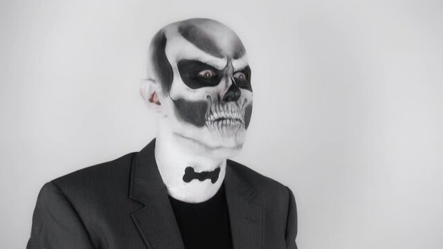 Halloween man in old skeleton make-up in business suit waddles. Shooting in the studio. Gray background