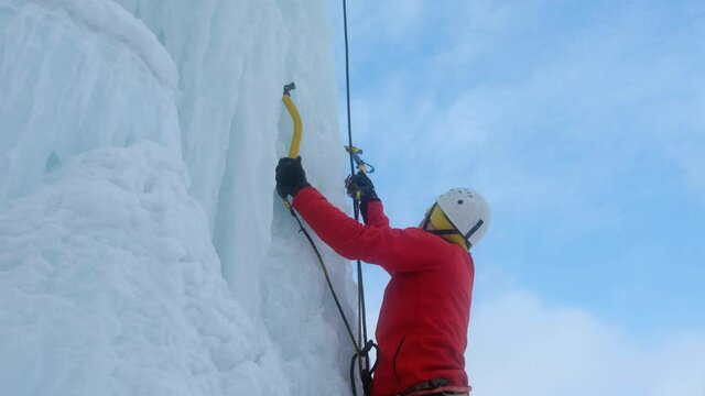 Alpinist man with ice tools axe climbing a large wall of ice.