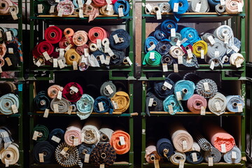 Big rolls of colorful fabric stacked on factory shelves ready for production