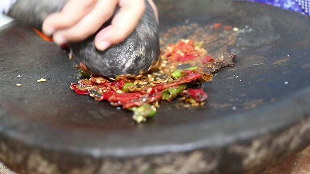 kneading chili sauce, a mixture of various spices, chilies, shallots, garlic, salt, flavorings, sugar and shrimp paste on a stone mortar