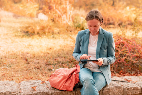 Woman using digital tablet on park bench in autumn