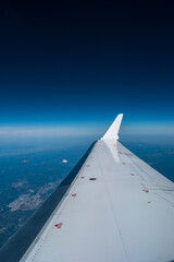 Fototapeta na wymiar Airplane window view of blue sky and earth with visible white wing in frame
