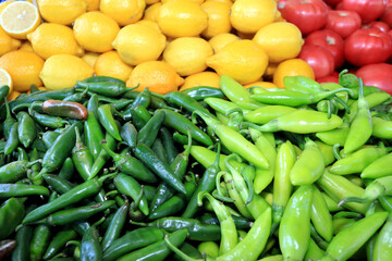 Green hot chili peppers, yellow lemons and red tomatoes in natural light. Colorful food pattern
