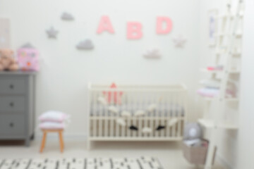Blurred view of cute baby room interior with modern crib near white wall