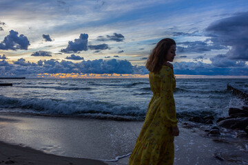 Russia, Kaliningrad region, Baltic Sea, girl silhouette at sunset at dusk in a long yellow dress.
