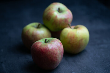 five red and green apples in front of black background