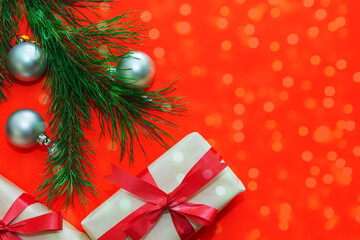 Christmas gifts are wrapped in white paper and tied with a red ribbon, fir branches are arranged on a red background. New Year and Christmas concept. Bokeh effect applied