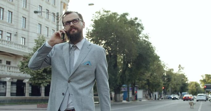 a business man with a beard and a phone in his hand walks down the street.