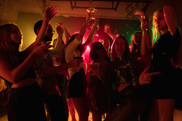 Emotion. A crowd of people in silhouette raises their hands, dancing on dancefloor on neon light...