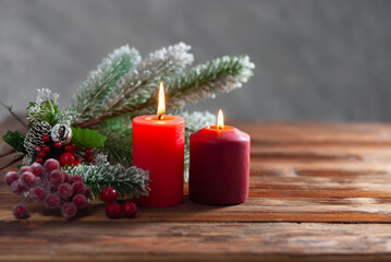 Two christmas red burning candles and branch of christmas tree on the wooden background Winter holiday xmas and new year