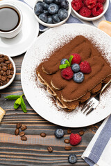 portion of Classic tiramisu dessert with raspberries and blueberries, savoiardi cookies and cup of espresso coffee isolated on wooden background