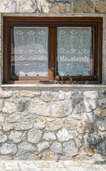 simple wooden frame window with white curtains and rough stone wall