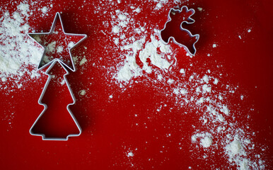 cutters for baking in the shape of a christmas tree deer and stars sprinkled with flour on a red background top view        