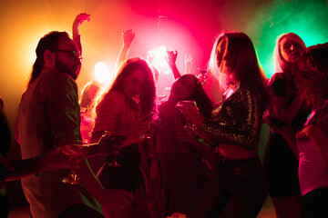 Energy. A crowd of people in silhouette raises their hands, dancing on dancefloor on neon light...