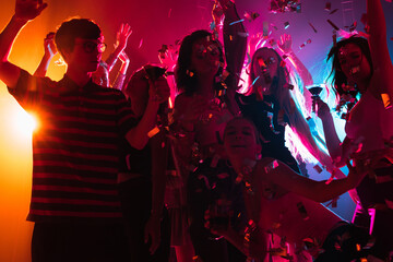 Confetti. A crowd of people in silhouette raises their hands, dancing on dancefloor on neon light background. Night life, club, music, dance, motion, youth. Bright colors and moving girls and boys.