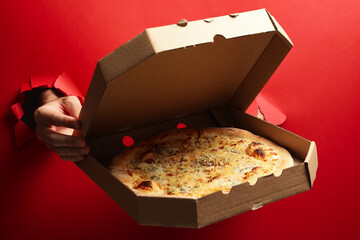 Hands hold box with tasty pizza on red background