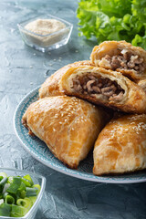Juicy samsa on a blue plate. Samsa with meat and onions. Samsa sprinkled with sesame seeds.