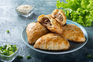 Juicy samsa on a blue plate. Samsa with meat and onions. Samsa sprinkled with sesame seeds.