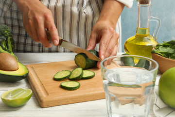 Woman cutted cucumber on white wooden table