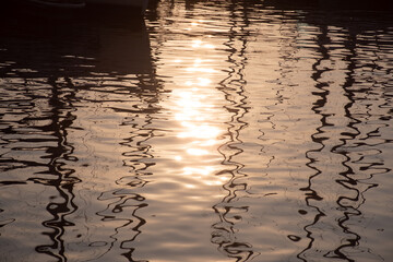 Reflections of sun and masts of a sailing vessel on the water, out of focus or blurred sea background