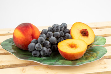 whole and cut fresh peaches and a bunch of grapes on a green leaf shaped plate

