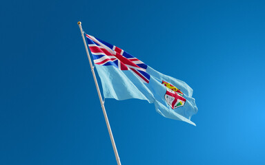 Isolated Fiji flag waving in the wind against blue sky background. Fiji national flag close up