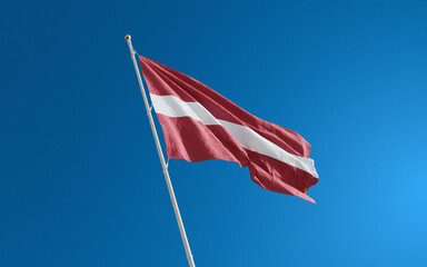Isolated Latvia flag waving in the wind against blue sky background. Latvia national flag close up
