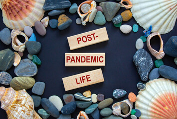 Text 'post-pandemic life' on wooden blocks on a beautiful black background. Sea stones and seashells. Concept.
