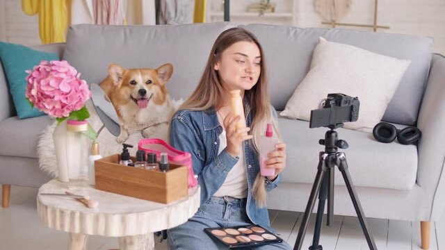 Attractive Teenager Girl With Her Cute Dog Vlogging About Makeup and Cosmetics.Young Girl Shooting Her Beauty Videoblog. Young Girl Conduct Remote Teaching to Сosmetic Сare During Blogging.