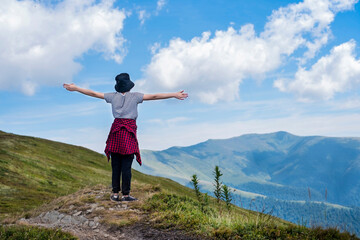 In the beautiful summer mountains, a young girl raised her hands and enjoys the strength and freedom of the mountains. Teen girl facing the mountains