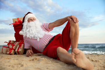 Obraz premium Santa Claus with bag of presents relaxing on beach. Christmas vacation