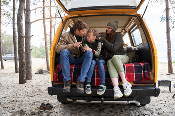 Family sitting on car trunk in the nature