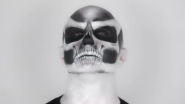 Man in horrible Halloween skeleton makeup posing for the camera. Shooting in the studio. Gray background