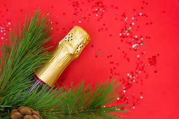 Fir xmas tree branch and bottle of champagne on a red background. Christmas and New Year concept. top view with space for text.